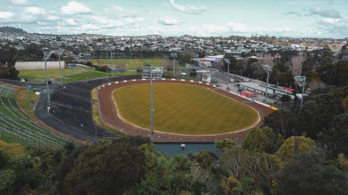An aerial view of the Western Springs stadium. The damaged boundary wall is in the left corner of this image, obscured by the trees. The damaged car park is to the top right, and the clubrooms in the centre-right.
